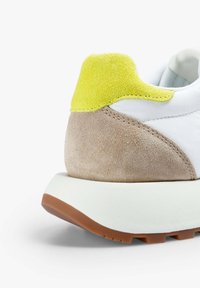 Sneaker bianca con accenti beige e gialli, dotata di controcanto in camoscio, superfici testurizzate e suola in gomma spessa con un motivo di battistrada.
