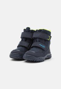 Sötétkék bokacsizmák dupla tépőzáras pántokkal, textil és szintetikus anyagokból, gumitalpakkal és kontrasztos neon zöld béléskiemelésekkel.