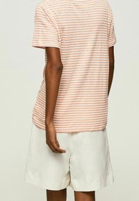 Gestreept T-shirt in licht perzik en wit, van katoen, korte mouwen, ontspannen fit, gecombineerd met witte linnen shorts. Geen opmerkelijke details.