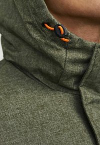 Zeleni ovratnik jakne v ribji kost, z teksturirano površino. Ima oranžno vrvico in črno zanko na vratu.