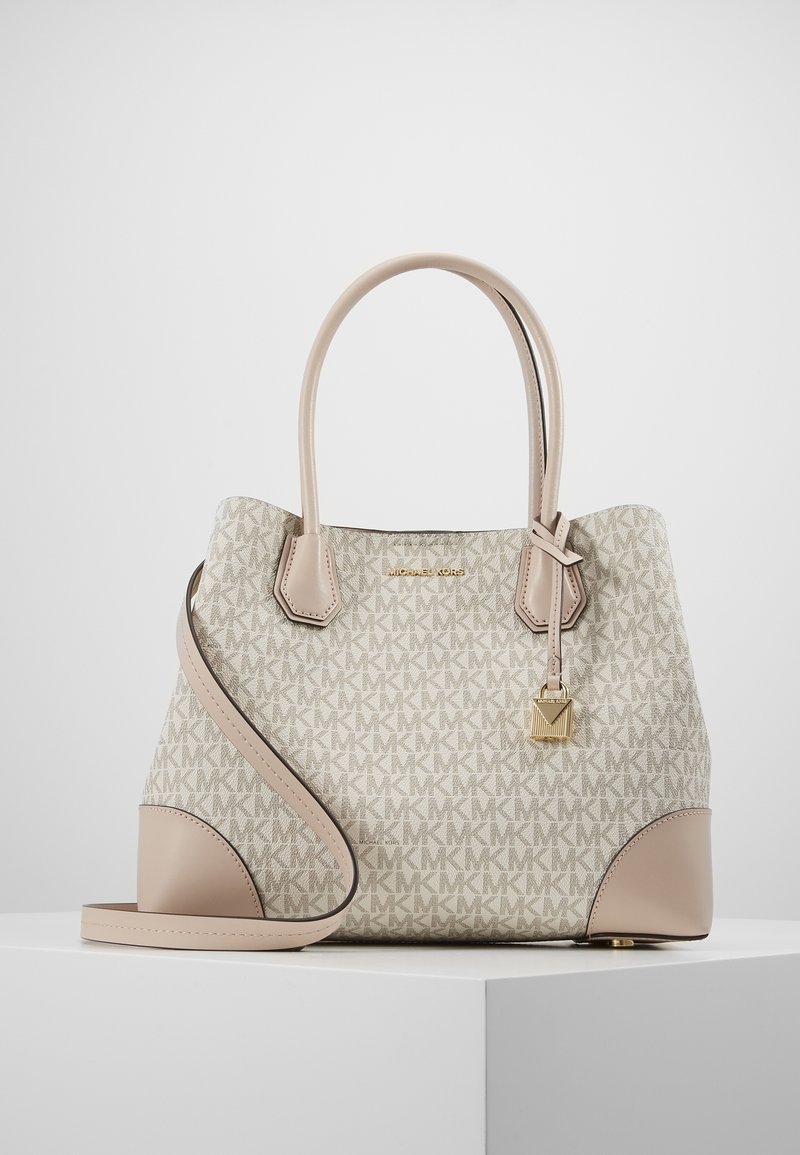 Sac à main beige et crème avec double poignée, bandoulière, breloque cadenas doré et motif répétitif du logo MK sur une surface blanche.
