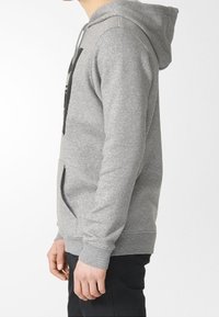 Felpa con cappuccio grigia realizzata in tessuto morbido, con tasca frontale e polsini a coste. Il design include un logo sul petto.