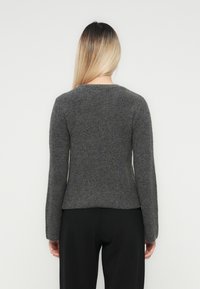 Un pull gris côtelé avec un col arrondi et des manches longues, fabriqué dans un matériau tricoté cosy, présentant une silhouette ajustée.