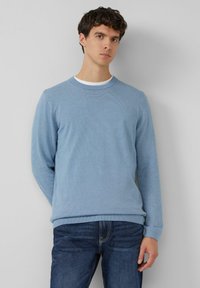 Hellblauer, gerippter Pullover mit rundem Ausschnitt und langen Ärmeln, kombiniert mit dunklen Jeans. Der Pullover hat eine strukturierte Oberfläche und enganliegende Bündchen.