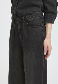 Pantaloni in denim nero a vita alta con gambe dritte, dotati di tasche frontali, cuciture a vista e chiusura classica con bottone e cerniera.