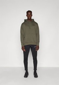 Felpa con cappuccio color verde oliva con tasca a marsupio e logo nero "PARIS". Pantaloni jogger neri aderenti con logo Nike, abbinati a scarpe da ginnastica nere.