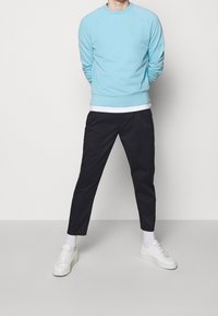 Lichtblauwe trui met lange mouwen, ribbelmanchetten en een ronde hals, gecombineerd met zwarte cropped broek en witte sneakers.