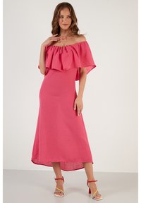 Väri off-the-shoulder vaaleanpunainen mekko, jossa on rypytyskerros, teksturoitu kangas ja haihtuva A-linjainen siluetti, yhdistettynä monivärisiin nauhakenkiin.