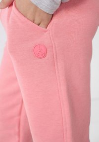 Roze katoenen joggers met een zijzak en een ronde gebosseleerde logo met "JOTT" aan de voorkant. Soepele structuur en een relaxte pasvorm.