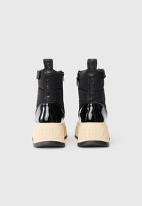 Zwarte gewatteerde high-top sneakers met glanzende zwarte accenten, beige rubberen zolen en een getextureerd logo op de achterkant. Ritsafsluiting detail.