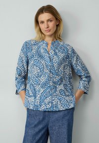 Bluse mit blau-weißem Muster, V-Ausschnitt, Dreiviertelärmel und lockerer Passform. Der Stoff hat ein strukturiertes, leichtes Aussehen.