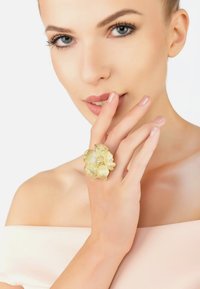 Gold-plated ring designed as a textured flower, featuring detailed petals and small decorative accents, worn on a finger against a light background.