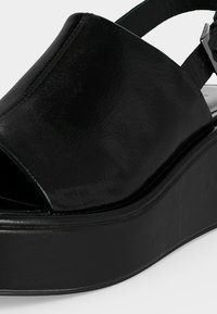 Μαύρο πέδιλο πλατφόρμα με σφήνα, ανοιχτή μύτη και λουράκι στον αστράγαλο με κούμπωμα.