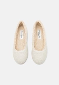 Chaussons en feutre gris clair avec une doublure douce en fourrure beige et un bout rond. Présente un design minimaliste et une étiquette de marque à l'intérieur.