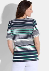 T-shirt à manches courtes, rayé bleu marine et blanc avec des accents verts. Tissu doux, coupe décontractée, encolure ronde, détails de couture visibles sur l'ourlet.