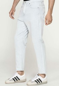 Jeans in denim azzurro chiaro con una vestibilità rilassata, caratterizzati da gamba dritta e cuciture decorative. Abbinati a sneaker bianche con righe nere.