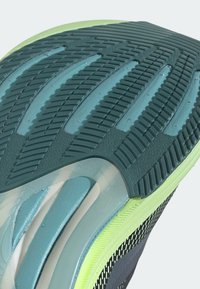Semelle de chaussure avec une accroche en caoutchouc texturé bleu sarcelle foncé, des rainures d’amorti translucides bleues et un bord de semelle intermédiaire vert clair.
