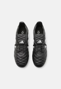 Scarpe da calcio nere con texture in pelle trapuntata, caratterizzate da accenti bianchi e un motivo a tre righe, logo rotondo sulla soletta nera.