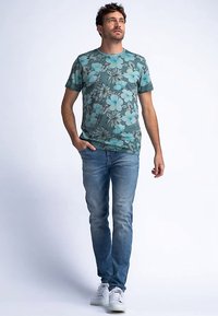 Tričko s krátkým rukávem v barvě modrozelené s květinovým vzorem v světle modré a béžové, doplněné světle modrými džínami a bílými teniskami.