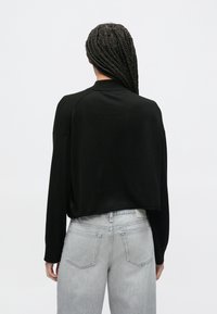 Maglione nero cropped con maniche lunghe, realizzato in un materiale morbido. Indossato sopra jeans grigio chiaro con un design classico a cinque tasche.