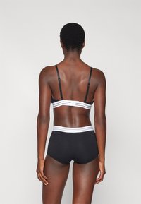 Conjunto de sutiã preto e cueca de cintura alta. O material é suave com detalhe em faixa branca. A vista de trás exibe alças ajustáveis.