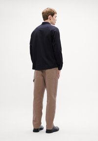 Svart långärmad skjorta med en texturerad mönster, i kombination med ljusbruna byxor med fickor, bärs tillsammans med svarta skor.