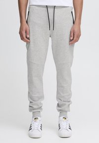 Grey sweatpants with a tapered fit, made of a soft fabric, featuring black zip pockets and a drawstring waistband. Worn with white sneakers.