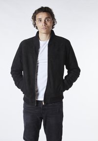 Svart mockajacka av bomberstil med dragkedja, ribbade ärmslut och krage. Bärs över en vit T-shirt och matchas med mörka jeans.