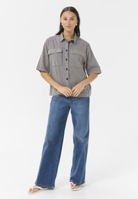 Chemise à manches courtes à rayures verticales noires et blanches, avec deux poches poitrine, associée à un jean en denim bleu à jambes larges.