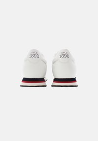 Sneakers bianchi con una finitura liscia, dotati di un collare imbottito, dettagli a strisce rosse e blu sulla suola e la scritta 'SINCE 1890' stampata sui talloni.
