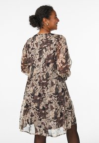 Abito floreale in beige, marrone e nero con maniche lunghe, vita arricciata e gonna a più strati. Realizzato in tessuto leggero e trasparente.