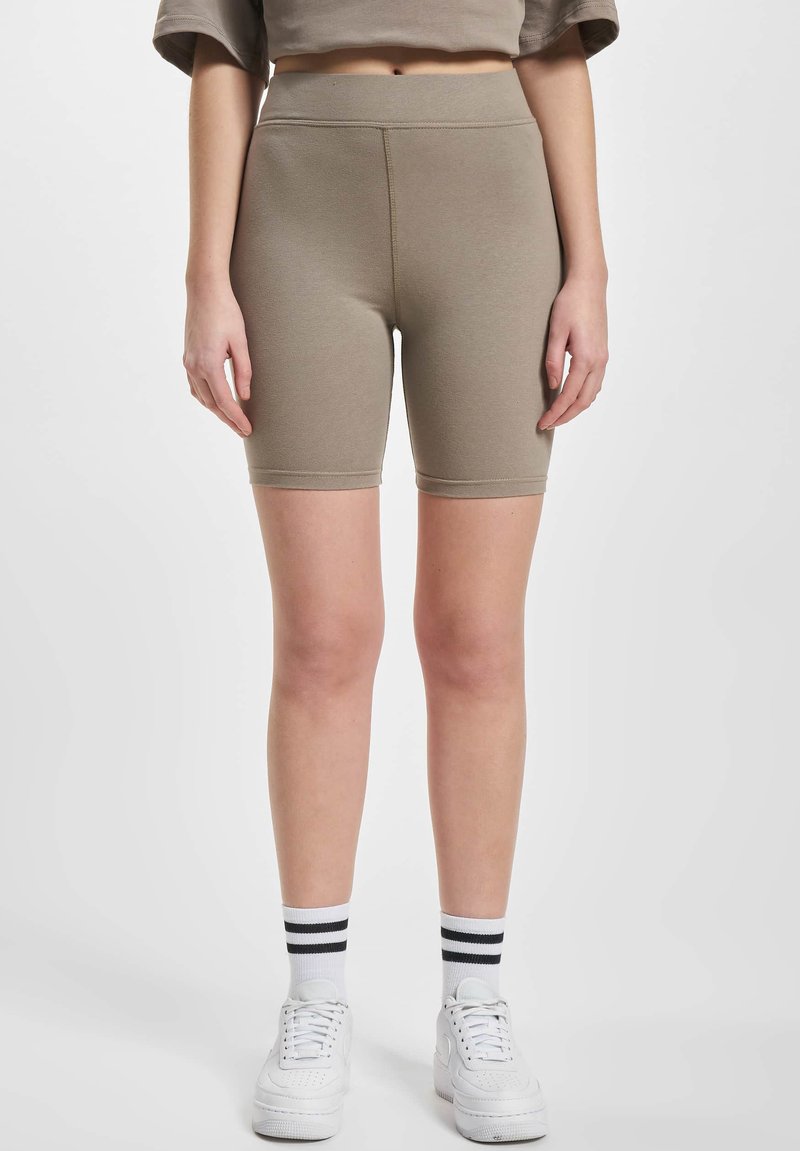 Khaki cyklistické kraťasy s vysokým pasem, vyrobené z pružné směsice bavlny. Hladká textura a design po kolena. Bílé tenisky s černými akcenty.