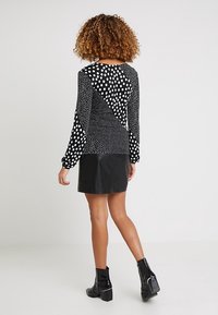 Czarna i biała bluzka z długim rękawem z wzorem kropek w różnych rozmiarach i trójkątnym wzorem. W połączeniu z czarną skórzaną mini spódniczką.