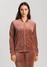 Sametová bomber bunda v jemně růžové barvě, s předním zipem, vroubkovanými lemy a hladkým povrchem. Stylizováno s odpovídajícími kalhotami.