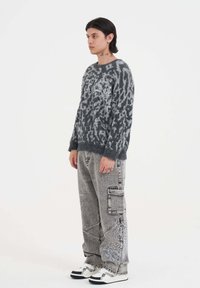 Grijze fuzzy trui met een luipaardprintpatroon, gecombineerd met grijze cargobroeken met witte borduursels, en zwart-witte sneakers.