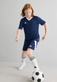 Tumes sinine spordiriietus valgete aktsentidega, sisaldab V-kaelusega särki, sobivaid šortse ja triibulisi jalgpall socks, koos must-valge jalgpalliga.