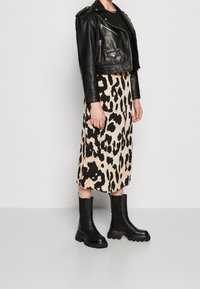 Chaqueta de cuero negra corta, falda midi de leopardo en beige y negro, y botas negras de suela gruesa, mostrando una mezcla de texturas y patrones.