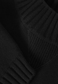 Tissu tricoté noir avec des motifs côtelés et texturés formant des formes géométriques sur la manche et le corps d’un vêtement.