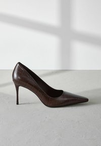 Brun lackläder högklackad pump med spetsig tå och alligatorprägling. Har en smal stilettklack.