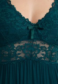 Teal pitsikoristeinen yömuoti, jossa on kukkakuosi, V-pääntie, satiininen nauhakoristelu ja pehmeä kangas, joka virtaa vyötärön alapuolella.