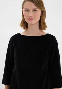 Haut noir à manches trois-quarts avec un large col arrondi. Texture douce, design minimal sans motifs ni détails visibles.