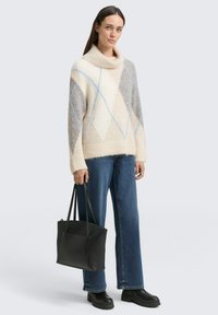 Pull en crème épais avec des motifs géométriques gris et bleu clair, associé à un jean bleu foncé et un sac fourre-tout noir. Bottes compensées noires.