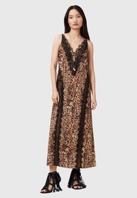 Abito maxi in stampa leopardata con bordi e dettagli in pizzo nero. Presenta una scollatura a V e spalline sottili. Abbinato a sandali neri con frange.
