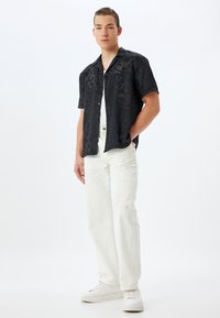 Camisa negra de manga corta con un patrón de remolino tonal, combinada con pantalones cargo blancos y zapatillas blancas. Tejido suave y corte relajado.