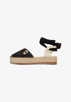 Alpargata en blanco y negro con suela de yute tejido, parte superior de tela y lazos para atar al tobillo. Patrón de cuadros notable en el talón y un pequeño detalle de logotipo.