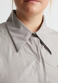 Hellgraues Hemd mit großem Kragen, Einfachknopfverschluss und strukturiertem Stoff. Verfügt über saubere Nähte und ein minimalistisches Design.