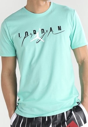 Mand iført en lyseblå Jordan T-shirt med sort-hvide shorts med lodrette striber og en rød lap.