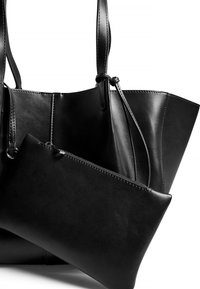 Svart läder tote-väska med en slät textur och strukturerad design, som har en mindre dragkedjeväska i samma material och färg.