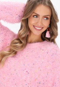 Puchaty różowy sweter z wielokolorowymi kropeczkami, okrągłym dekoltem i nieco oversizowym krojem. Charakteryzuje się miękką teksturą i długimi rękawami.
