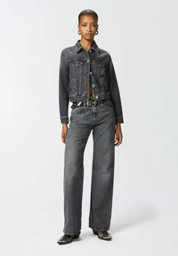 Tamna traper jakna sa skraćenim rukavima i prednjim džepovima, uparena sa širokim tamnim farmerkama. Outfit sadrži crni pojas sa srebrnim metalnim detaljima.